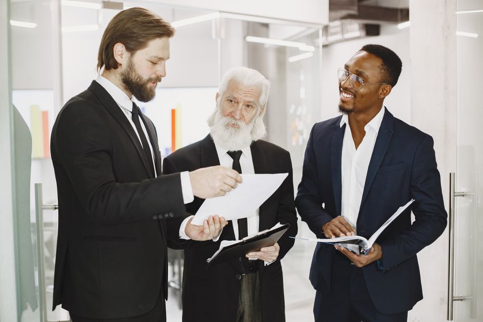 Three businessmen in suits discussing documents in a modern office setting.